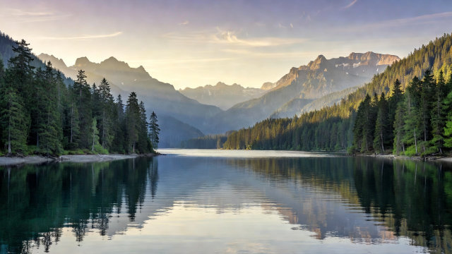 An Alpine lake stretching between forested shores beneath a layered mountain skyline.